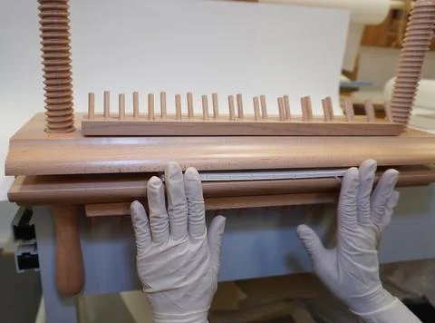 Gloved hands install a block of sheets in a wooden bookbinding press. Stock Photos