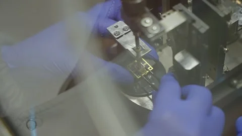 Gloved hands manipulate a microelectronic component with tweezers on a precision Stock Footage 325975849