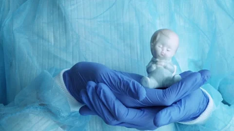 Gloved hands, midwives or nurses hold a statuette of a small child. Stock Footage 302913385