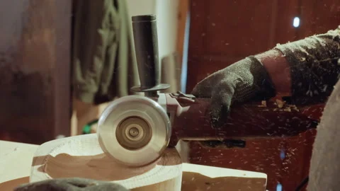 Gloved hands operating angle grinder on wooden block wood shavings flying in Stock Footage 348119401