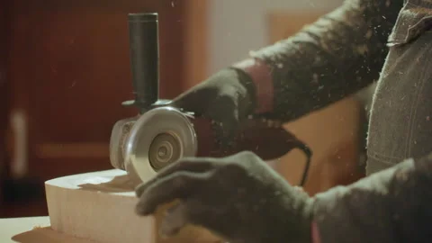 Gloved hands operating angle grinder on wooden block with sawdust flying in Stock Footage 348119405