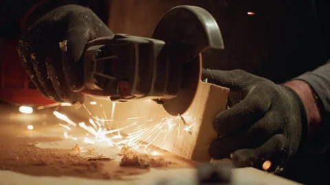 Gloved hands operating angle grinder to cut wood with sparks flying showing Stock Footage 348121259