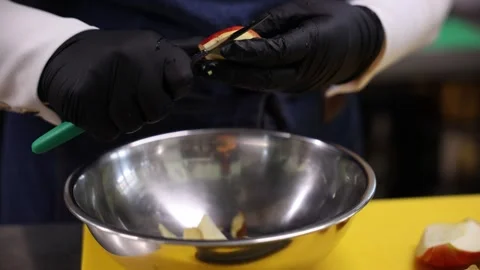 Gloved hands peel and slice apple over stainless bowl in kitchen Stock Footage 337582297