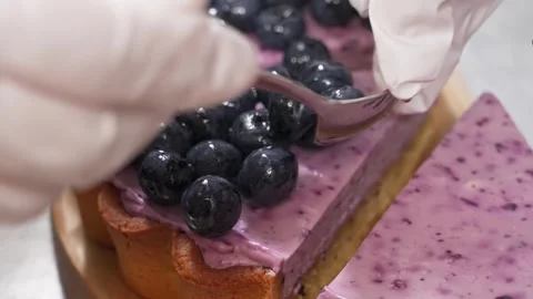 Gloved hands placing fresh blueberries on top of a purple berry custard tart. Stock Footage 337751205
