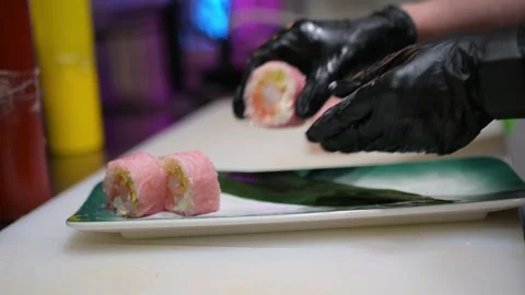 Gloved hands placing sliced pink sushi rolls with colorful filling on a Video stock 293507501