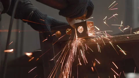 Gloved hands position metal bracket beside grinding tool in dim workshop with Vídeo Stock 347017041