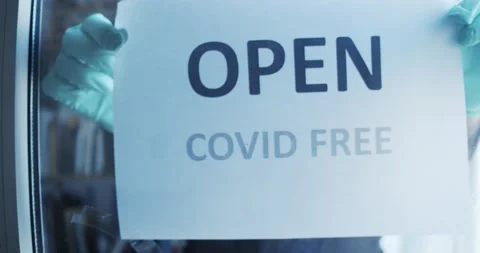Gloved hands put up a sign in a store with the phrase "open, free covid". Stock Footage 131175807