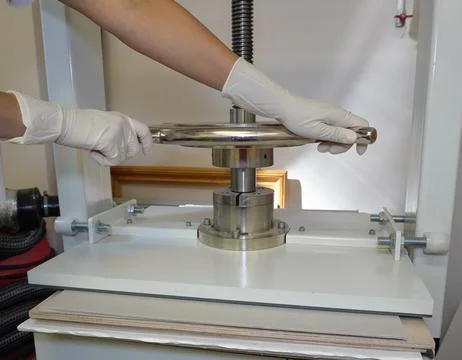 Gloved hands rotate the handle of the screw press. Foto stock