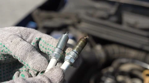 Gloved hands of serviceman comparing old and new spark plug during car repair Stock Footage 306855601