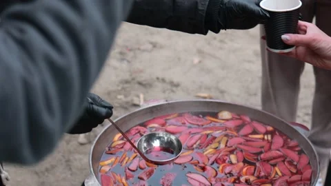 Gloved hands serving warm fruity mulled drink with ladle from large pot at Stock Footage 300206535