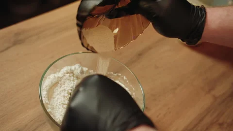 Gloved hands skillfully move dry yeast into glass bowl Video stock 330536552