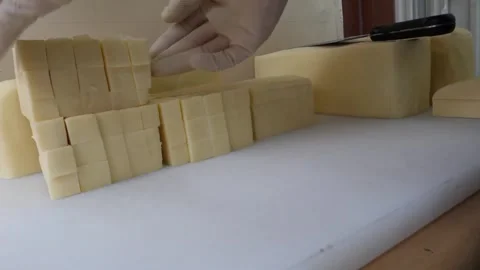 Gloved Hands Slicing and Arranging Blocks of Yellow Cheese on White Cutting Boar Video stock 343587527