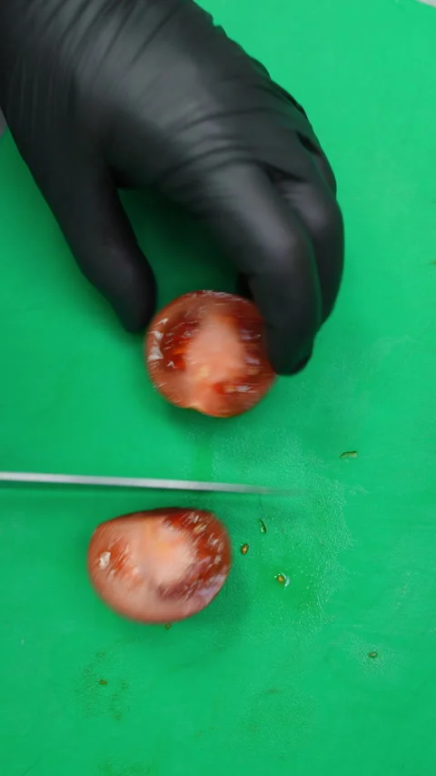 Gloved hands slicing ripe red tomato into segments atop green cutting board 스톡 동영상 309130264