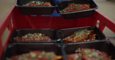 Gloved hands stacking black trays of marinated meat garnished with chives into Vídeo Stock 340000337