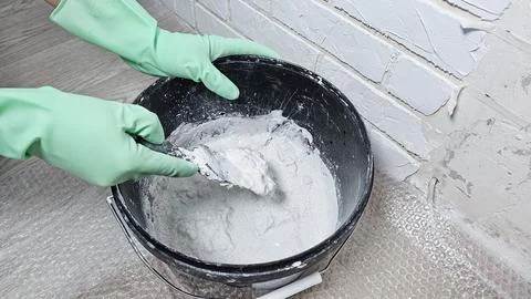 Gloved hands stir the putty, cement with a spatula in a bucket Stock Photos