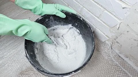 Gloved hands stir the putty, cement with a spatula in a bucket Stock Photos