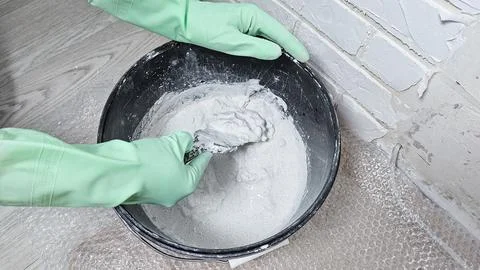 Gloved hands stir the putty, cement with a spatula in a bucket Stock Photos
