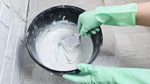Gloved hands stir the putty, cement with a spatula in a bucket Stock Photos