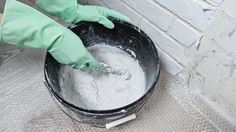 Gloved hands stir the putty, cement with a spatula in a bucket Stock Photos