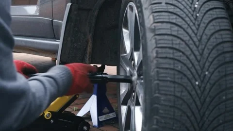 Gloved hands tightening wheel nuts with lug wrench during passenger car wheel Stock Footage 341568914