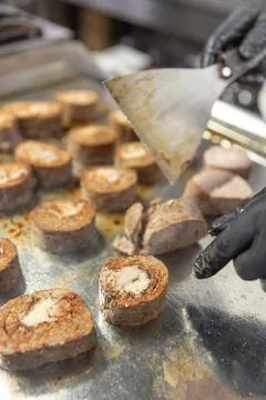 Gloved hands using a spatula arranging freshly cooked meat Stock Photos