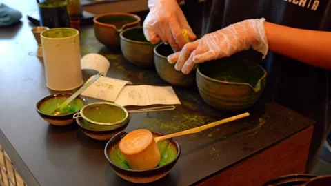 Gloved hands whisking matcha in ceramic bowl at tea counter. Close view of green Stock Footage 336339200