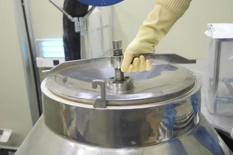 Gloved kitchen worker opens the lid of a stainless food cooking vessel. Stockfoto's