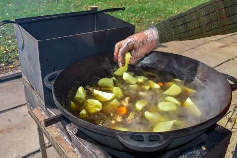 A gloved man's hand throws potatoes into the broth. Boil the broth with meat and Stock Photos