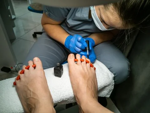 Gloved master makes a pedicure for a client. close-up no face. woman in a nail Stock Photos