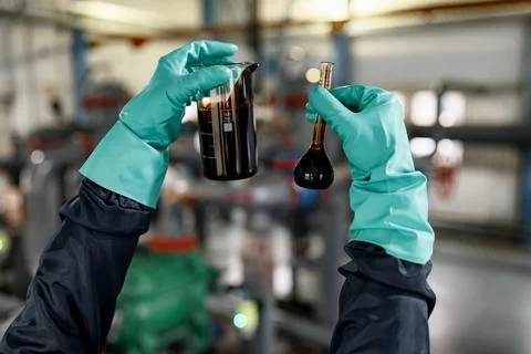 Gloved petroleum laboratory technician comparing dark liquid samples in glass Foto stock