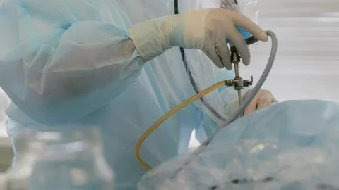 Gloved surgeon hands adjusting endoscopic instrument with clear tubing during Photos