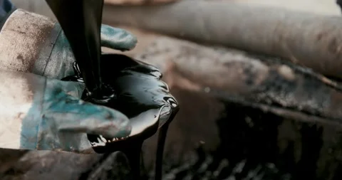 Gloved worker catches thick black industrial liquid dripping from a pipe in 스톡 동영상 346315416