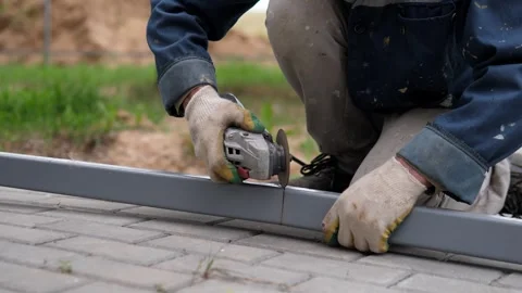 Gloved worker grinding gray metal bar outdoors with handheld tool, bright sparks Stock-Footage 344824308