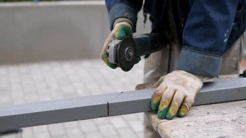 Gloved worker grinding gray metal beam with handheld angle grinder outdoors Stock-Footage 344872459