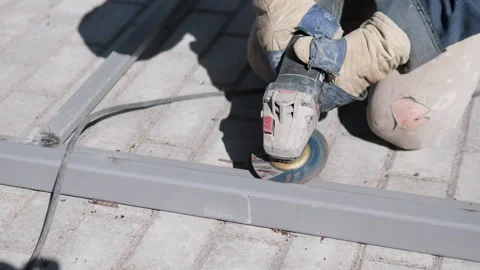 Gloved worker grinding gray metal beam with handheld tool on bright concrete Vídeo Stock 347692432