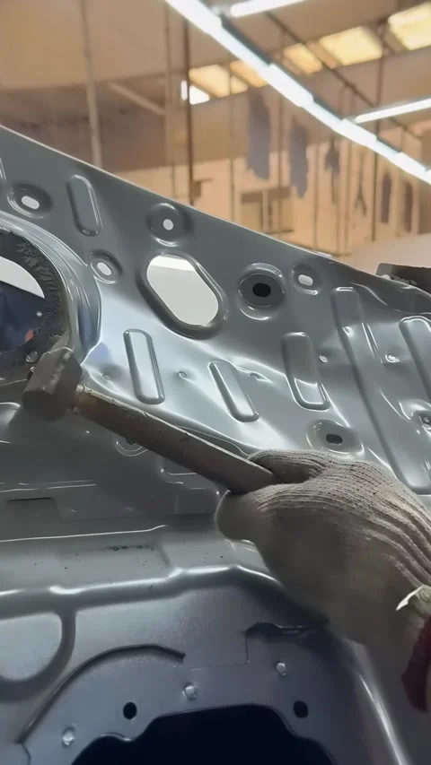 Gloved Worker Hammering Dent Out of Gray Car Body Panel in Workshop 動画素材 348691484