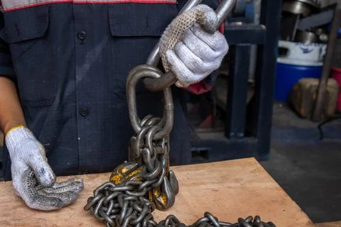 Gloved worker holds heavy lifting chain sling in industrial workshop. Foto stock