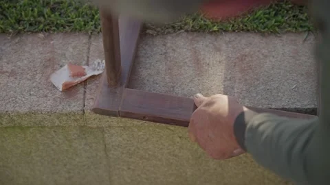 Gloved worker sanding wooden post base on outdoor paving stone Vidéo 333095739