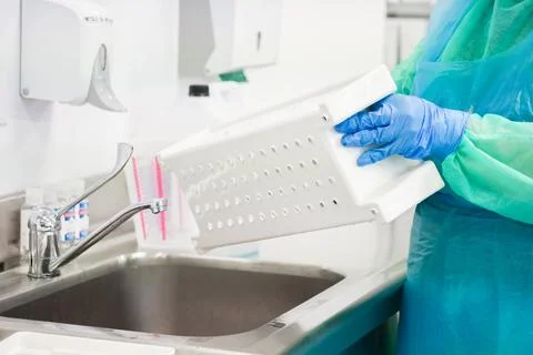 A gloved worker sanitizing a plastic basket at a sink in a medical facility.. Stock Photos