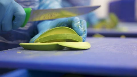 Gloved Worker Slicing Fresh Avocado on Sanitized Cutting Board 스톡 동영상 346738993