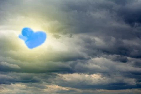 Glow through the clouds of the evening warm sun. Blue cloud in form of heart. 스톡 사진
