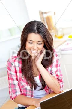 Glowing asian woman using her laptop sitting sitting in the kitchen Stock-Fotos