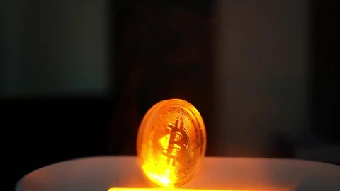 Glowing Bitcoin Coin on Surface, A glowing Bitcoin coin standing upright on.. Stock Footage 304875533