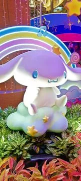 A glowing Cinnamoroll statue sits on a cloud before a neon rainbow Stock Photos
