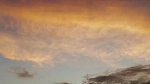 Glowing cloud across pastel sunset sky, soft orange and gold banding above dim Stock Footage 323437562