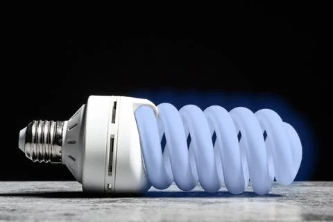 Glowing cold light fluorescent bulb on the grey table on black background Stock Photos