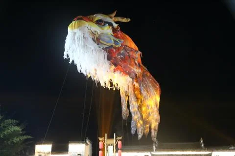 Glowing dragon puppet head and body suspended over traditional rooftops in .. Stock Photos