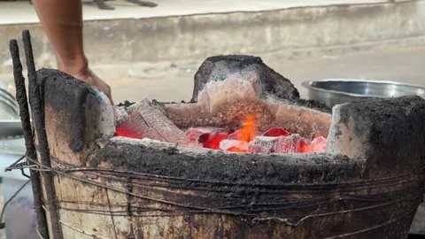 Glowing embers are moved between traditional clay stoves with long tongs, heat Stock Footage 331725831