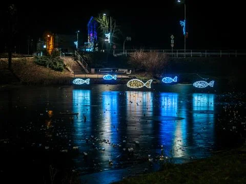 Glowing fish-shaped light decorations suspended over a reflective. Stock Photos