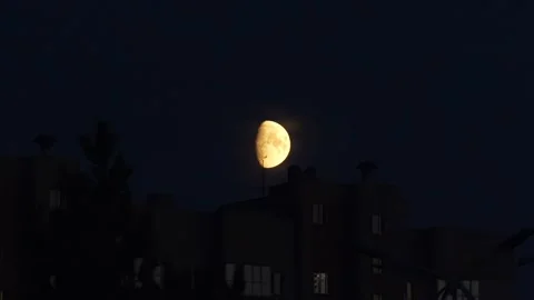 A glowing half moon rising above dark city buildings at night. Stock Footage 343240090